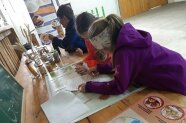 3 Kinder beugen sich über Papier auf einem Tisch